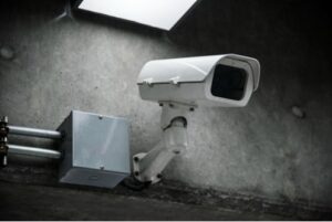 A bullet camera is positioned inside a facility on a concrete wall.