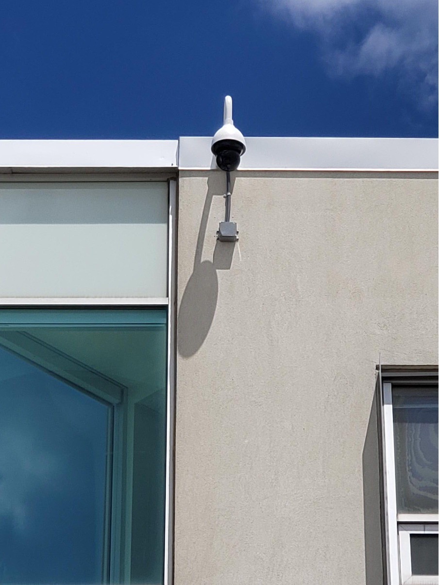 Close-up view of a dome camera set up outside on the side of a commercial building.